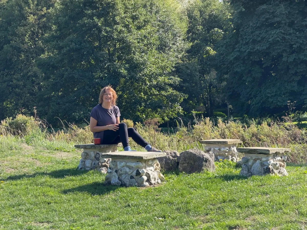 A guest sitting on a flint and stone bench in the sunshine on the lawn at West Lexham, with trees behind